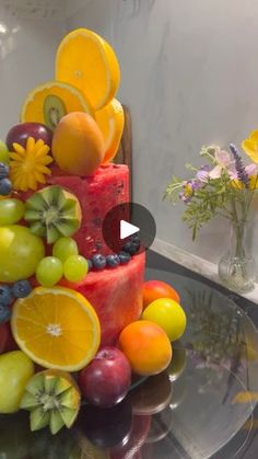 there is a cake made out of fruit and flowers on top of the glass table