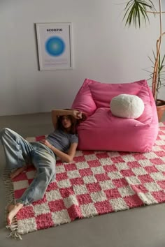 a woman laying on top of a pink bean bag chair next to a potted plant