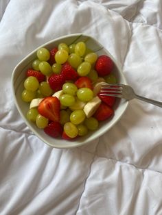 a white bowl filled with grapes, strawberries and cheese on top of a bed