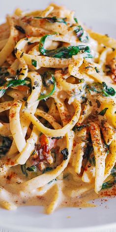 a white plate topped with pasta covered in sauce and spinach leafy toppings