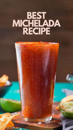 a glass filled with red liquid next to chips and limes on a blue table