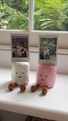 two marshmallows sitting on a window sill with pictures hanging from them