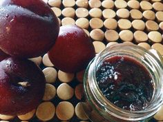 there are plums next to a jar of jam on a table with wooden circles