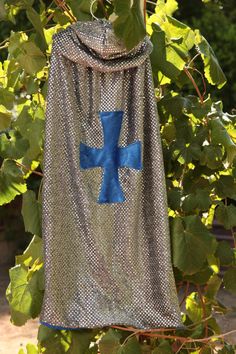 a blue cross on a silver blanket hanging from a tree with green leaves in the background