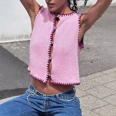 a woman sitting on the ground with her arms behind her head wearing a pink knitted top