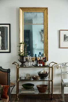 a bar cart with bottles and glasses on it next to a mirror in a living room