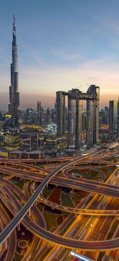 an aerial view of multiple roads in the middle of a city at dusk with tall buildings and skyscrapers