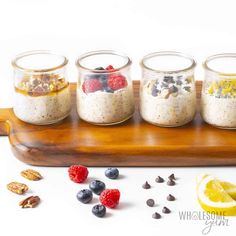 three jars filled with granola and fruit on top of a wooden tray next to nuts