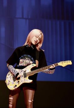 a woman holding a guitar while standing on stage