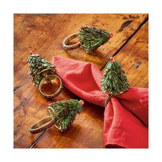 three napkin rings are sitting on top of a red cloth with pine trees in them