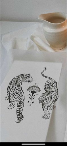 a white plate topped with a drawing of two tigers next to a cup and saucer