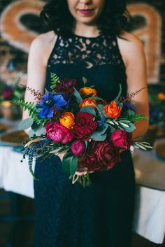 a woman in a black dress holding a colorful bouquet with red, orange and blue flowers