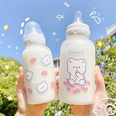 someone holding two baby bottles in front of a blue sky with white clouds and stars