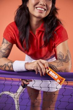 a woman with tattoos on her arm holding a bar of chocolate in front of a volleyball net