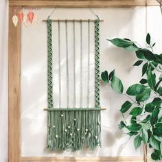 a green macrame hanging on a wall next to a potted plant and wooden frame