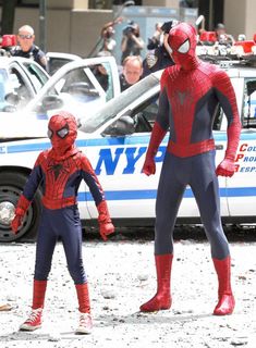 two children dressed as spider - man in front of a police car