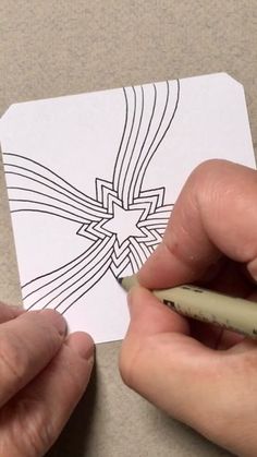 two hands holding a pencil and drawing a star on a piece of paper with black ink