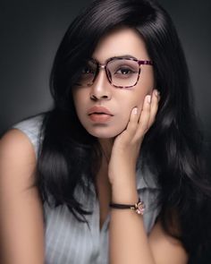 a woman wearing glasses is posing for the camera with her hand on her chin and looking off to the side