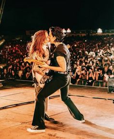 a man and woman kissing while playing guitar in front of an audience at a concert