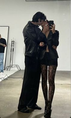 a man and woman standing next to each other in front of a mirror with their arms around each other