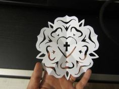 a person holding up a paper cut out of a heart with a cross on it