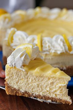 a person holding a piece of cheesecake on a plate with lemons and whipped cream