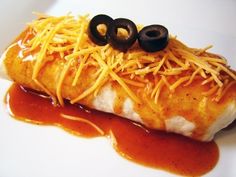 an enchilada covered in cheese and black olives on a white plate