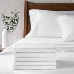 a stack of white sheets on top of a bed next to a vase with flowers