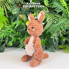 a small crocheted rabbit sitting in front of some green plants and leaves with the text, kangarooo pop pattern