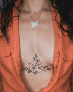 a woman wearing an orange shirt has a flower tattoo on her chest and is looking at the camera