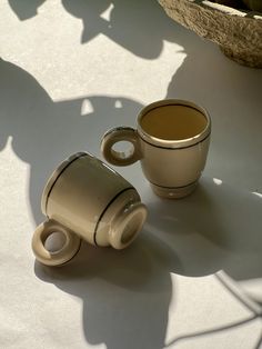 two coffee cups sitting next to each other on top of a white tablecloth covered floor