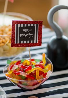 a bowl filled with gummy bears sitting on top of a striped table cloth next to a black kettle