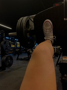 a person with their feet on a barbell in a gym area at night time