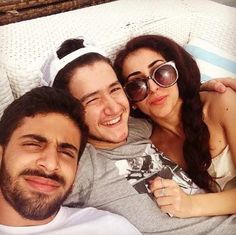 two men and a woman laying on a bed with their arms around each other smiling