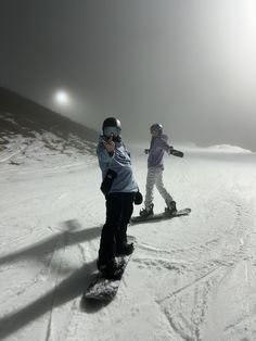 two children are snowboarding down a hill in the foggy day, one is holding his arms out