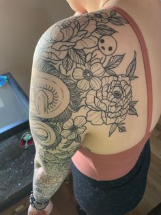 the back of a woman's shoulder with flowers and skulls tattooed on her arm