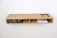 a wooden shelf with some books and magazines on top of it in front of a white wall