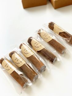 five cinnamon sticks wrapped in clear cellophane and labeled with writing on them sitting next to some brown boxes