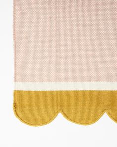 a pink and yellow rug with scallops on the edge, against a white background