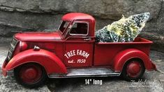 an old red truck with a christmas tree in it's bed on some rocks