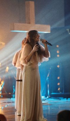 a woman standing on top of a stage with a microphone in her hand and other people behind her