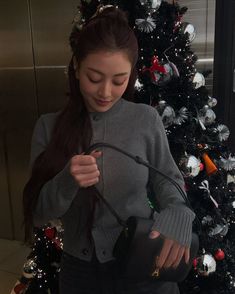 a woman holding a black purse in front of a christmas tree