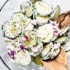 a glass bowl filled with cucumber salad and a wooden spoon in the bowl