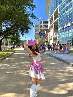 a woman in a pink hat and white dress posing for the camera with her arms up