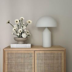 a white vase with flowers on top of a wooden cabinet next to a lamp and books