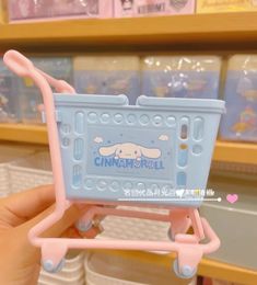 a person holding a toy shopping cart in front of shelves with other items on it