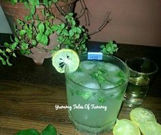 a glass filled with green liquid next to sliced lemons and mint leaves on a wooden table