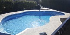 an above ground swimming pool surrounded by shrubbery and fenced in area with sun shining on the water