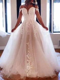 a woman in a white wedding dress standing on a wooden floor with her hands behind her back