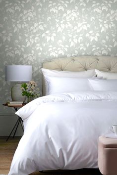 a bed with white sheets and pillows in a bedroom next to a wallpapered wall